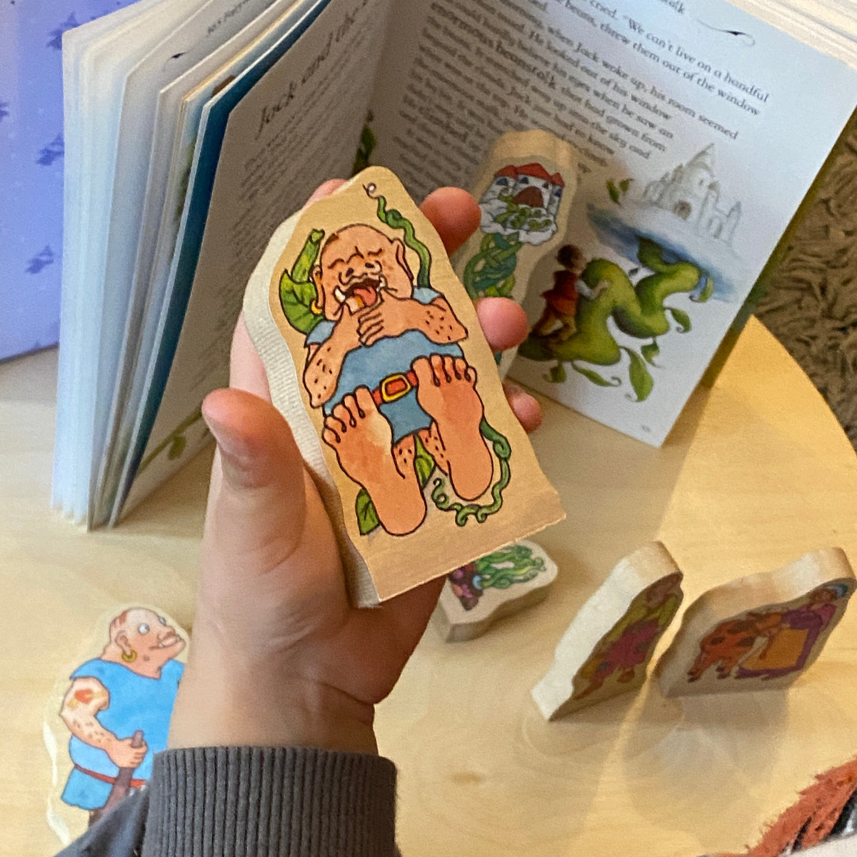 Hand holding a wooden story figure with a cartoon character next to an open book