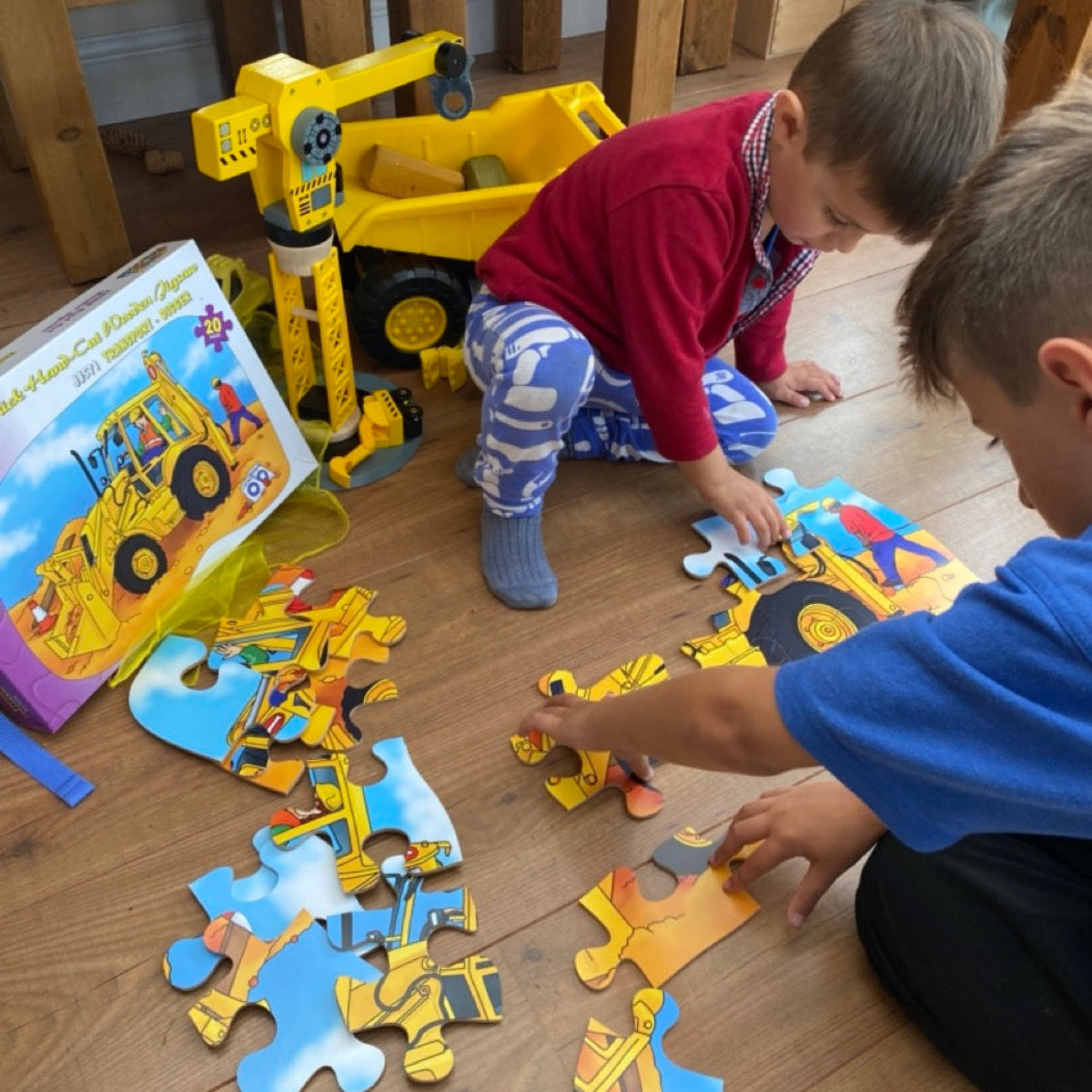 Two children playing with construction-themed digger puzzle pieces on a wooden floor.