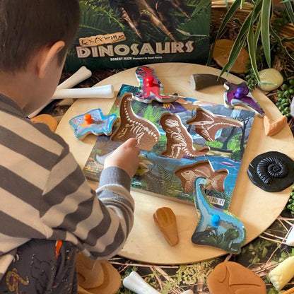 Child playing with dinosaur fossil toys and a box labeled 'Dinosaurs' on a table.