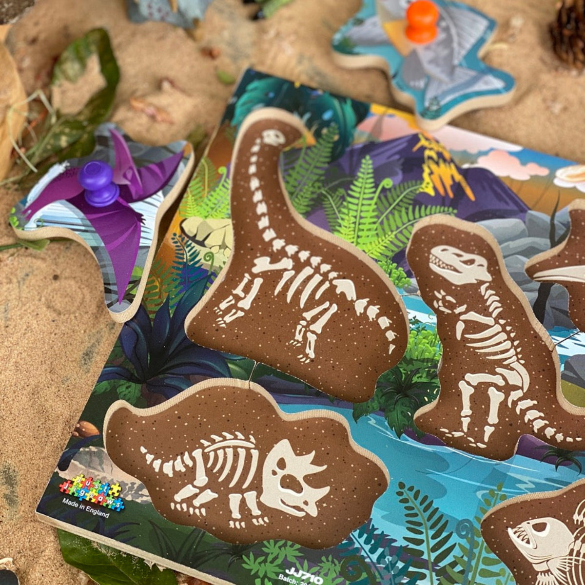 Dinosaur skeleton jigsaw peg puzzle on a sand-like surface with a colorful book in the background