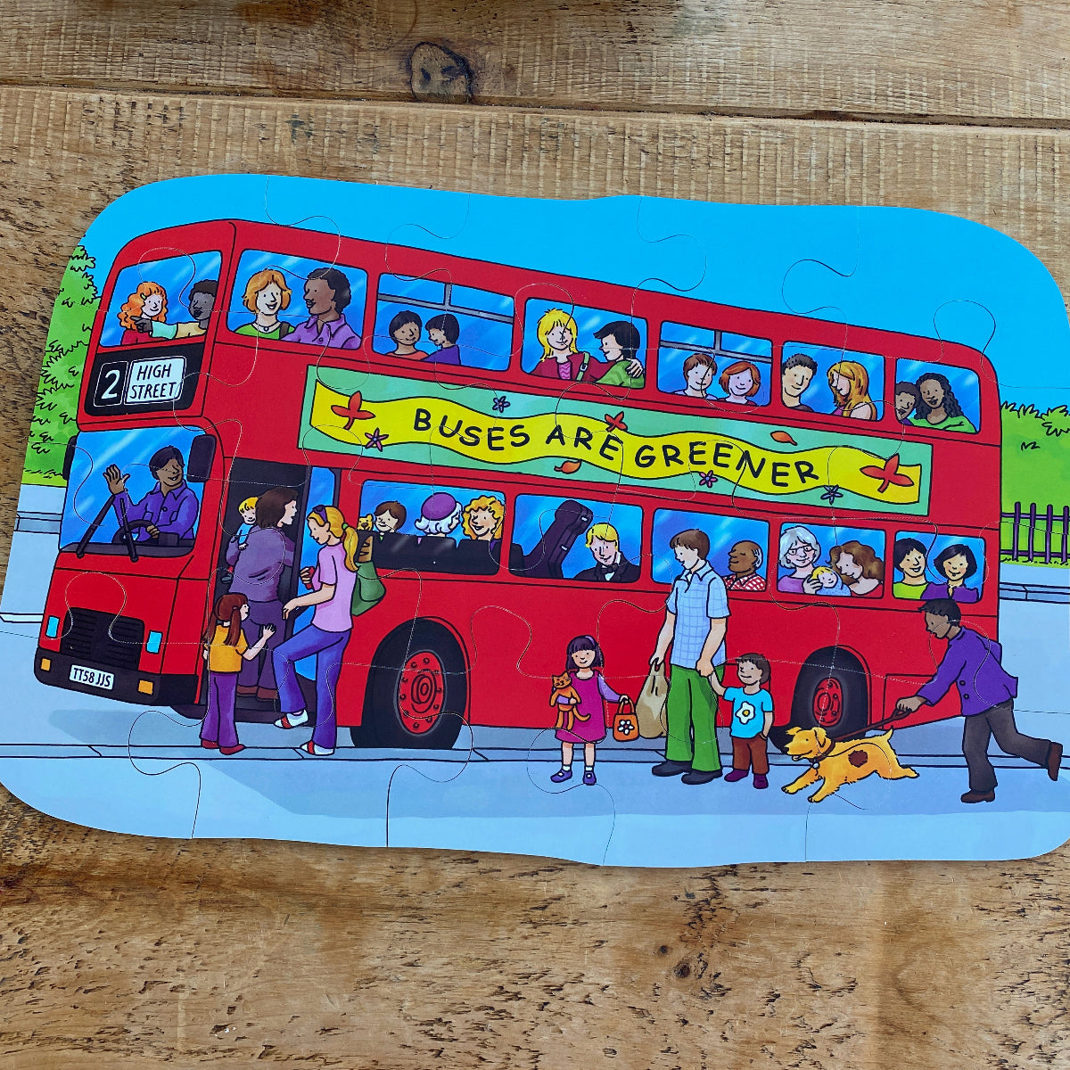 Children's puzzle with a red double-decker bus and people on a wooden surface