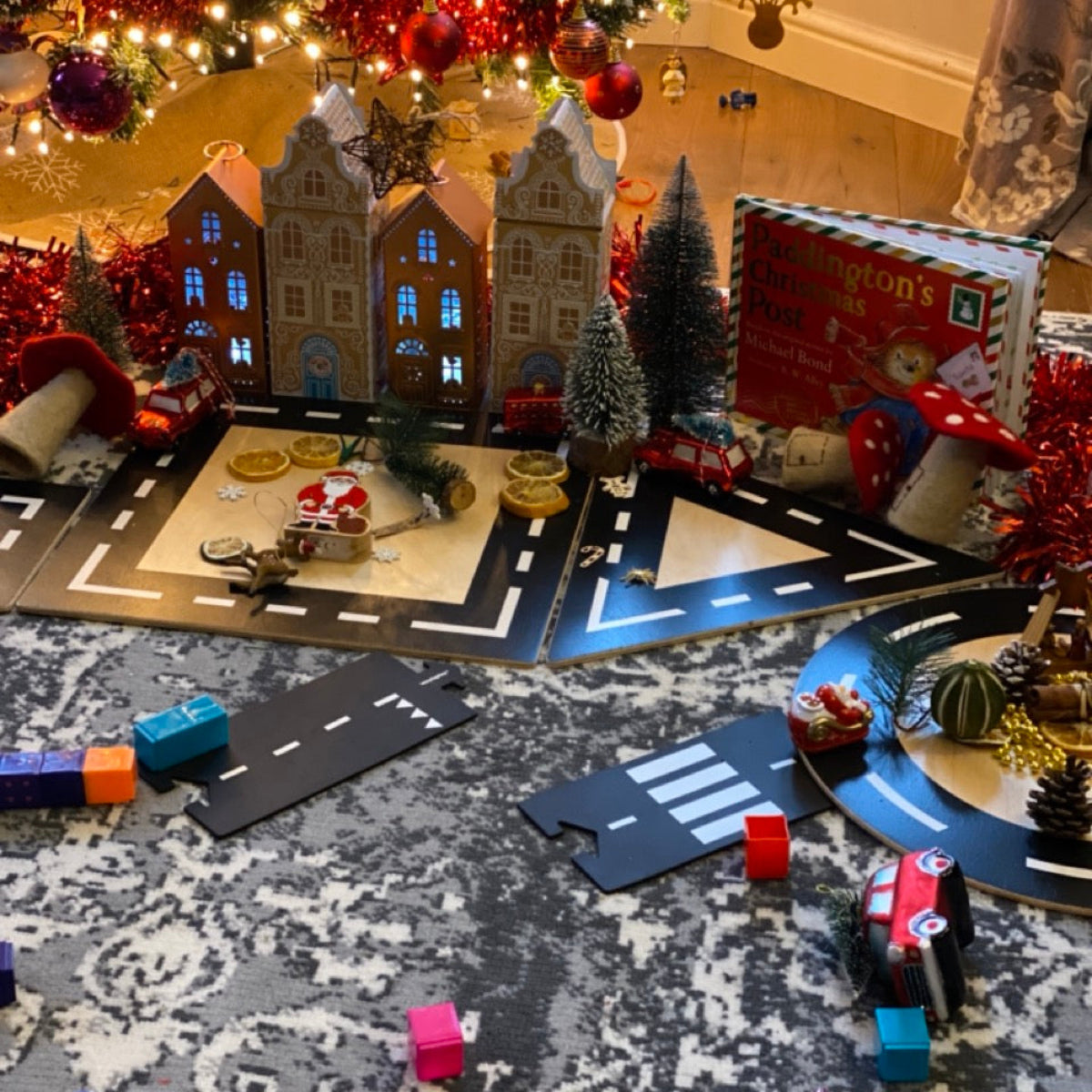 Children's toy set with miniature houses, cars, and Christmas decorations on a carpeted floor.