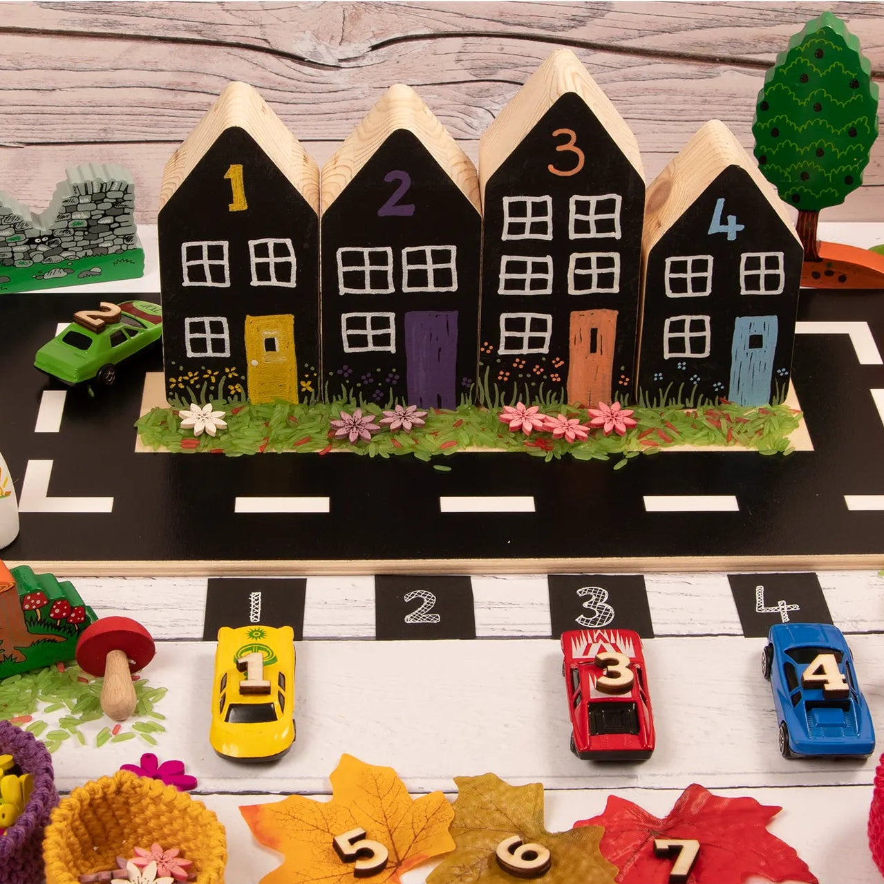 Toy town set with houses, cars, and decorative elements on a wooden surface.