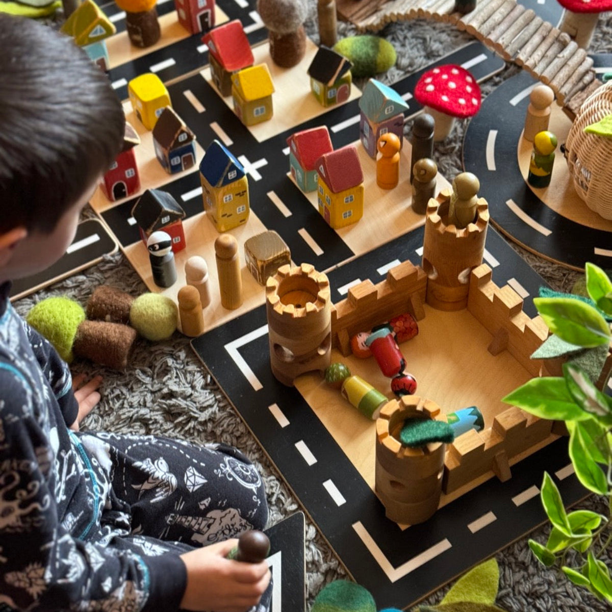 Child playing with a wooden toy set on a road mat