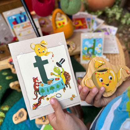 Child holding a card with a letter 't' and a toy figure, surrounded by educational materials.