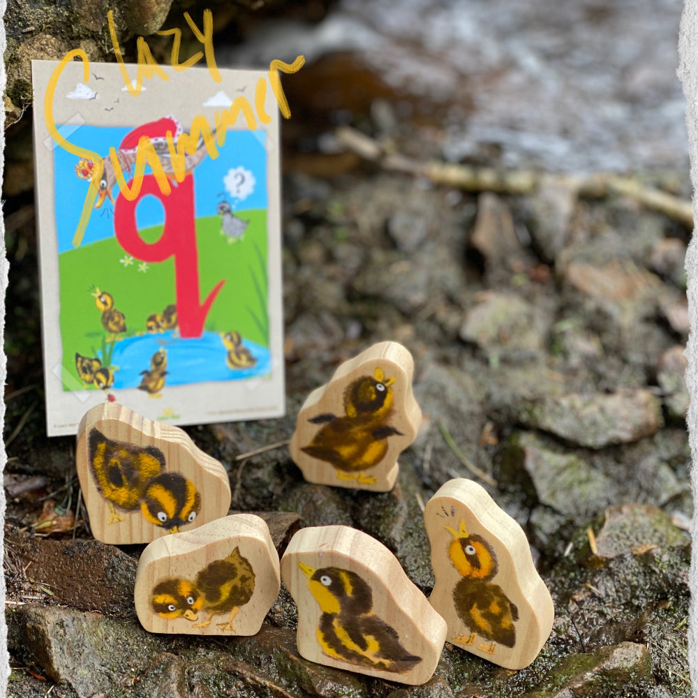 Wooden 5 little duck characters with a small card featuring a duck illustration on a stone background