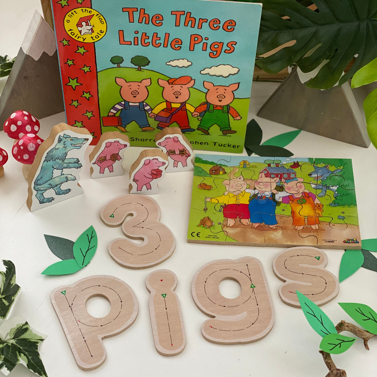 Educational children's toys and books about the Three Little Pigs on a white surface with plants.