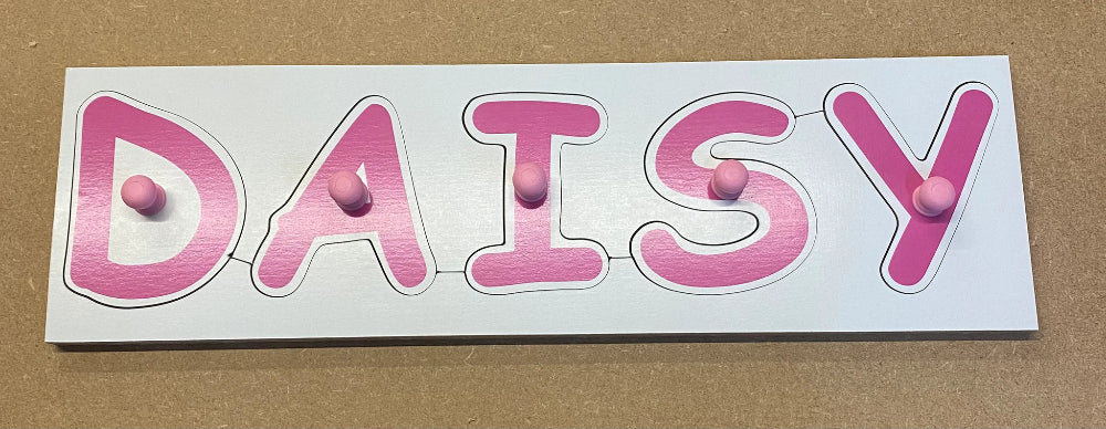 Wooden name plate peg puzzle with 'DAISY' in pink letters on a white background