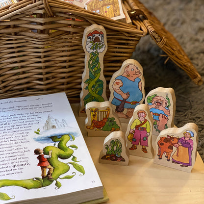 Wooden fairy tale characters next to an open book with illustrations on a wooden surface.