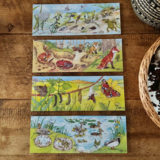 Set of nature-themed lifecycle jigsaw puzzles on a wooden surface with a woven basket. Frog, Fox, Butterfly and Duck.