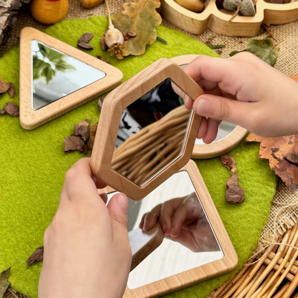 Person holding a small wooden mirror with nature-themed decorations on a textured surface.