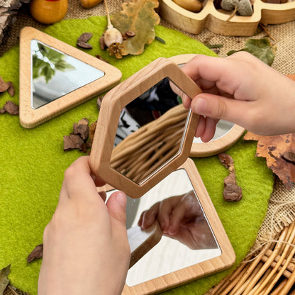Person holding a small wooden mirror with nature-themed decorations on a textured surface.