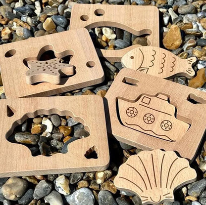 Wooden toy shapes with starfish, fish, shell, and boat designs on a pebble background
