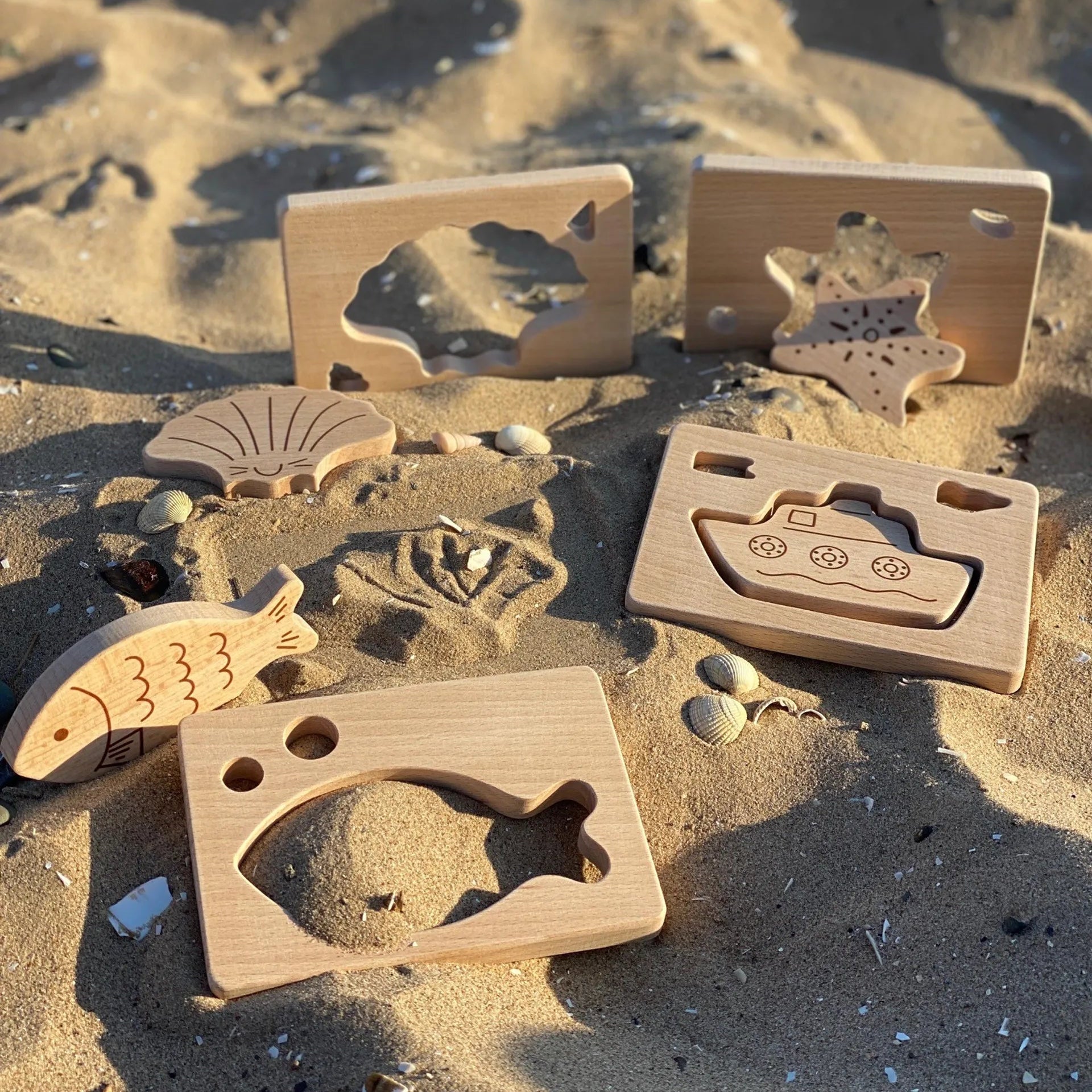 Wooden toys shaped like shells, starfish, boats and fish on a sandy beach
