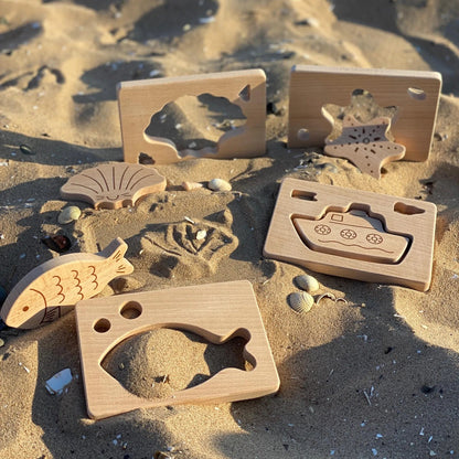 Wooden toys shaped like shells, starfish, boats and fish on a sandy beach
