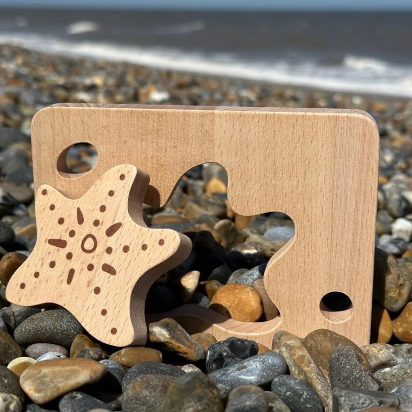 Wooden Starfish shape puzzle piece on pebbles with ocean in the background
