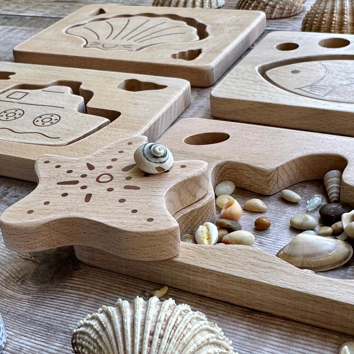 Wooden puzzle with shell designs on a wooden surface with seashells and stones.