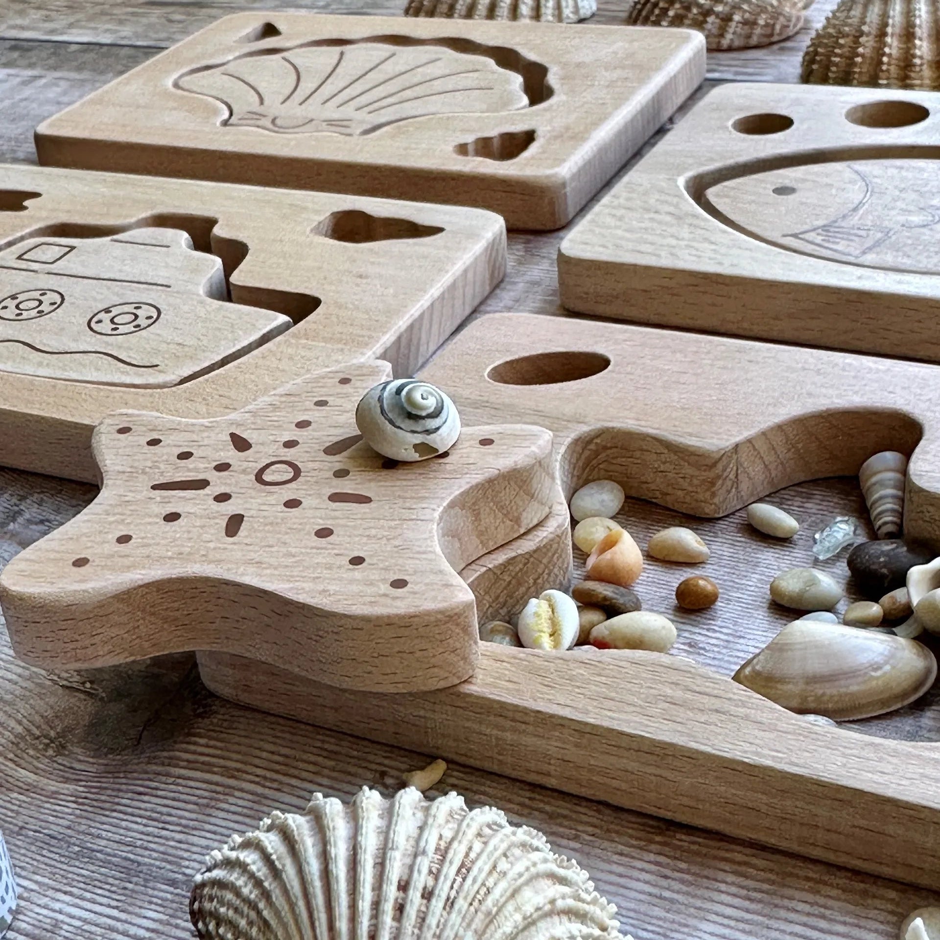 Wooden puzzle with shell designs on a wooden surface with seashells and stones.