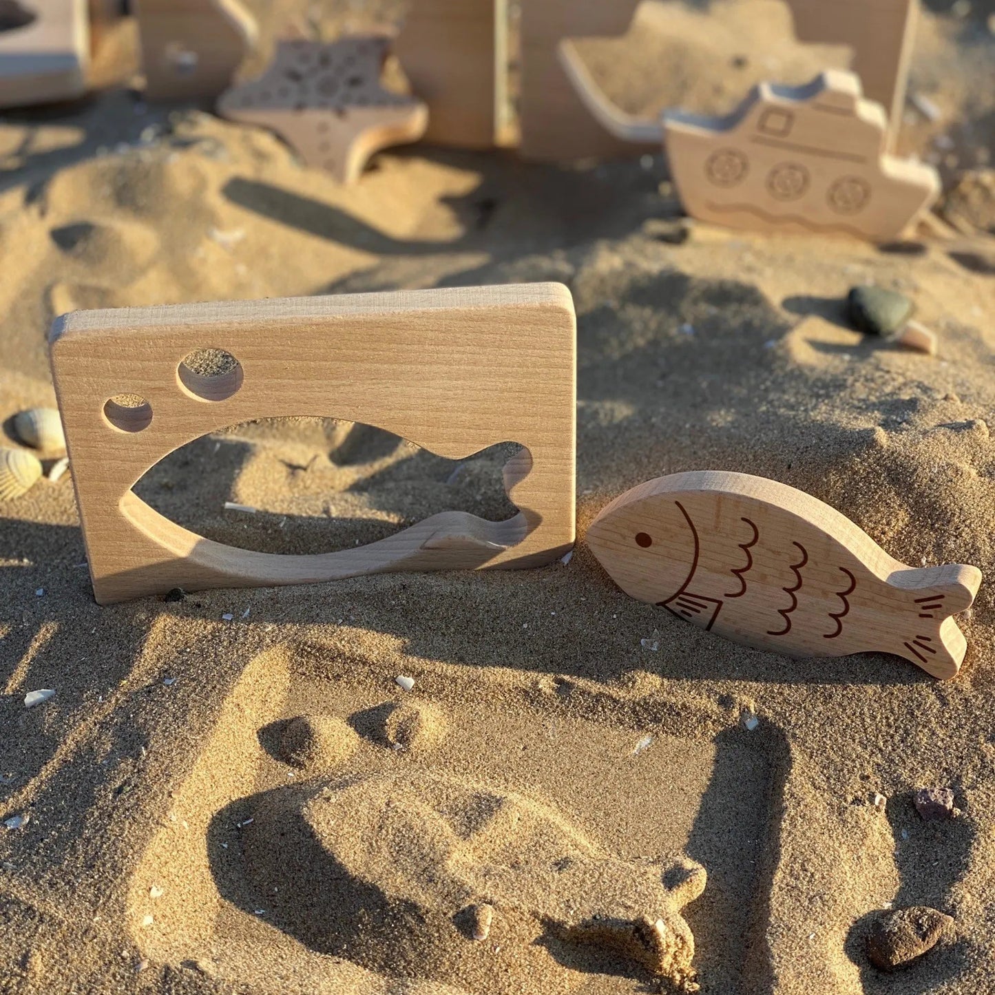Wooden toys shaped like a fish and a castle on a sandy surface