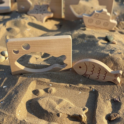 Wooden toys shaped like a fish and a castle on a sandy surface