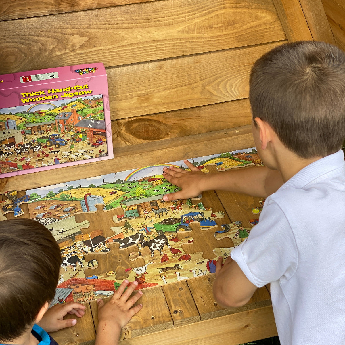 Two children playing with a puzzle on a wooden floor.