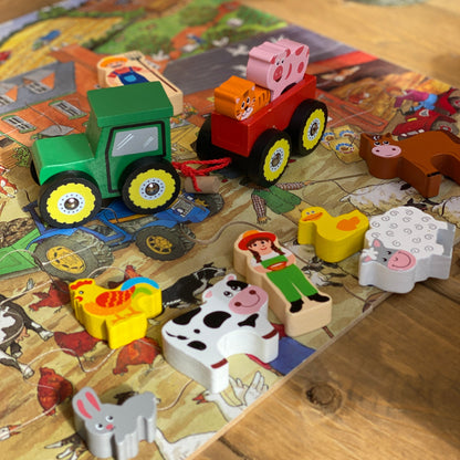 Wooden farm animal toys on a wooden surface with a colorful puzzle in the background.