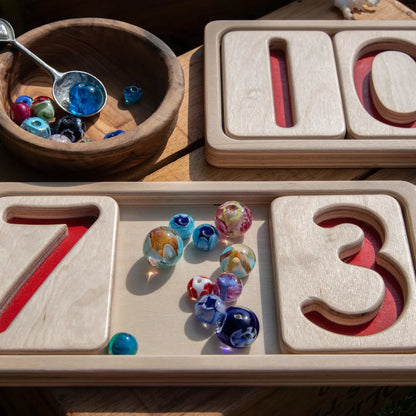 Wooden number trays with colorful beads on a wooden surface. Counting loose parts