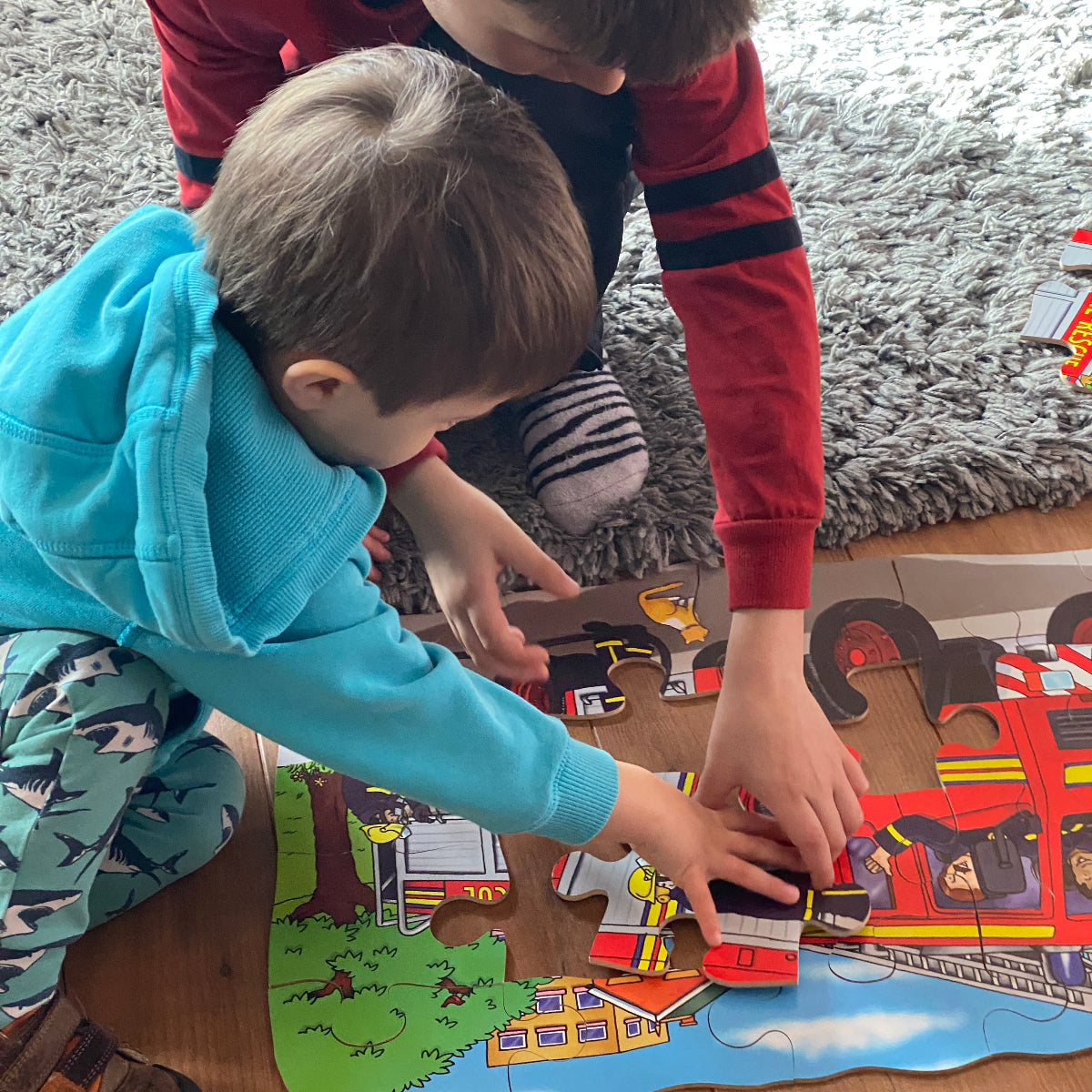 Two children playing with toys on a colorful play mat. Fire engine jigsaw.