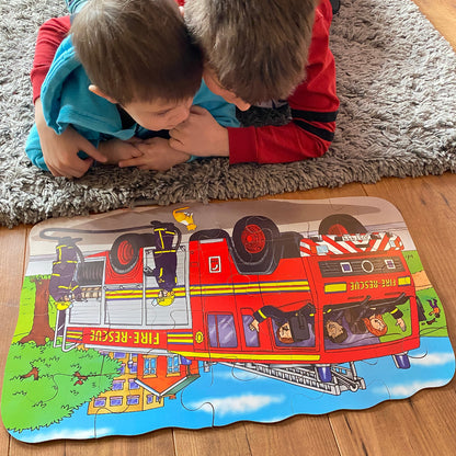 Two children playing with a fire truck puzzle on a wooden floor.