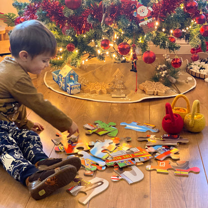 Child playing with jigsaws on the floor next to a decorated Christmas tree.
