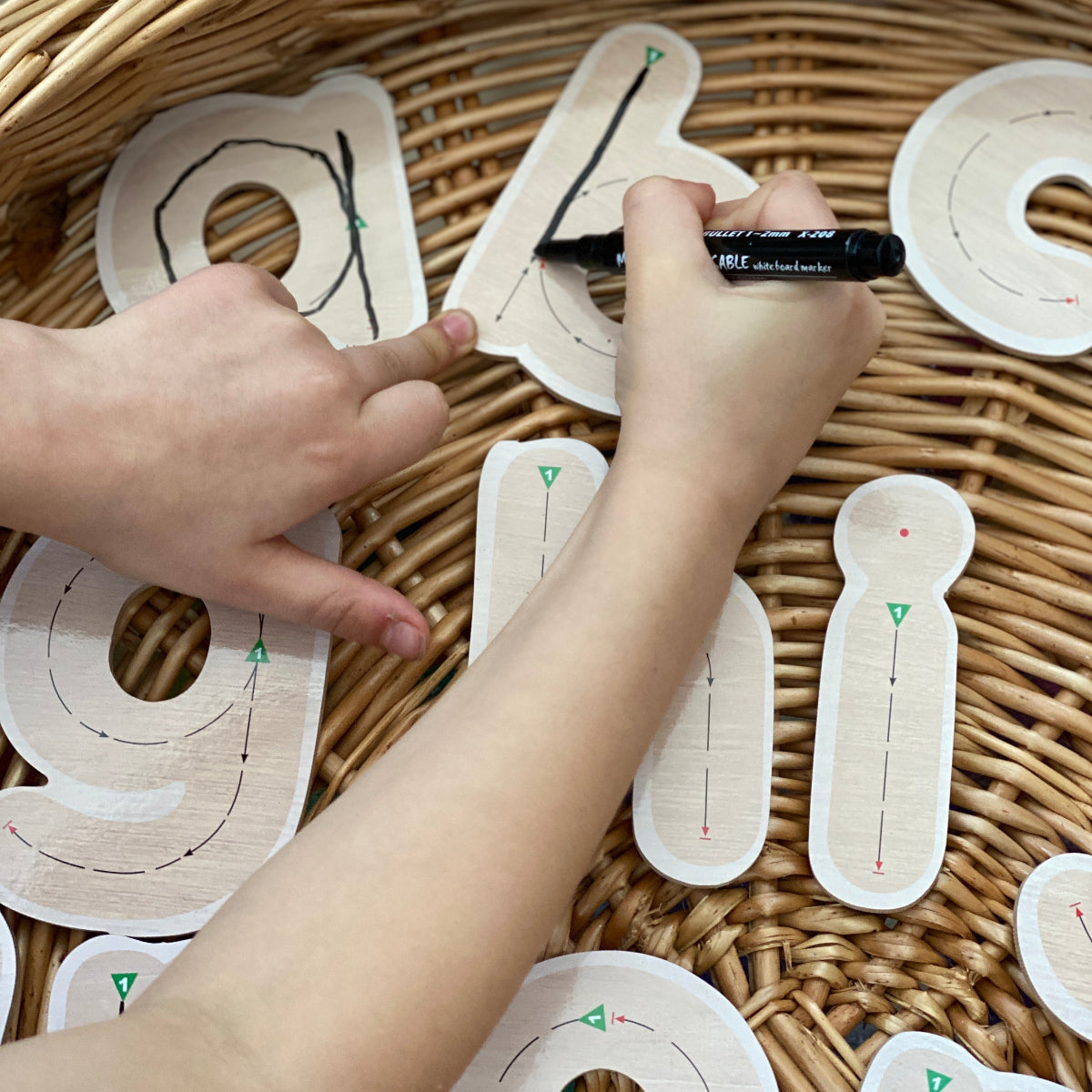 Children's hands using a marker to draw on wooden letters.