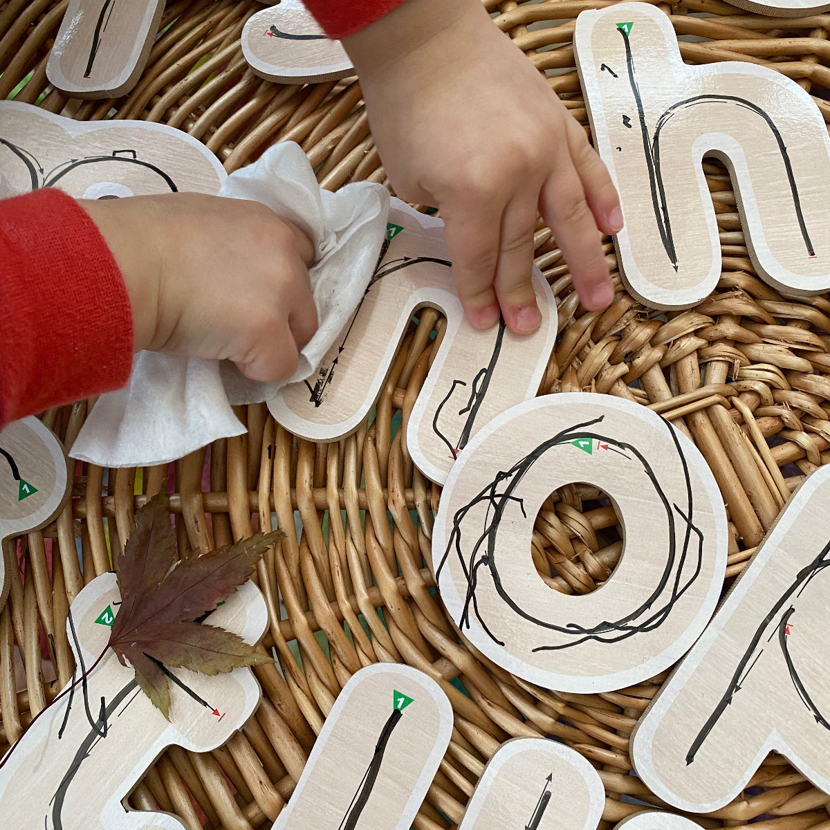 Children's hands interacting with educational wooden letters on a wicker surface - wipe clean