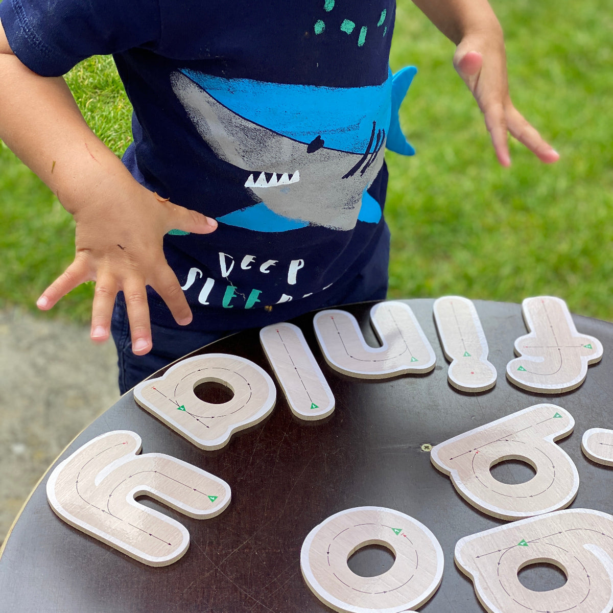 Child playing with letter tiles on a tray outdoors