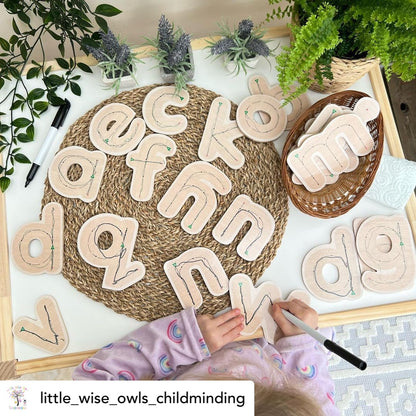 Children's hands playing with wooden letters on a table with plants in the background