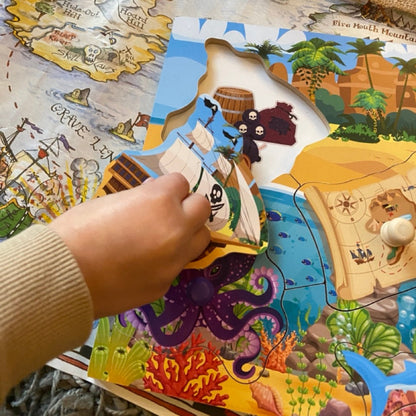 Child playing with a pirate ship toy on a children's book with a map and pirate-themed illustrations.